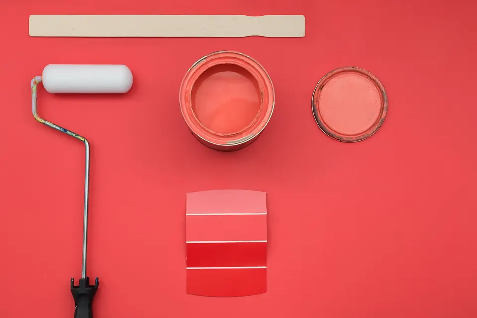 A tin of coral paint, a roller and colour cards on a coral background