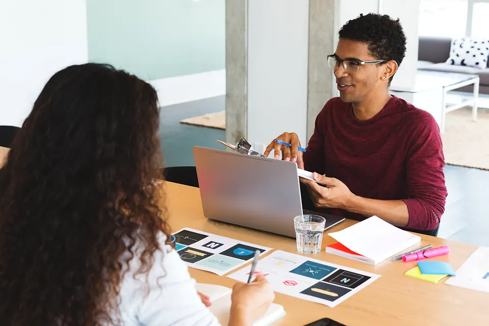 Two people talking over logo designs at a table