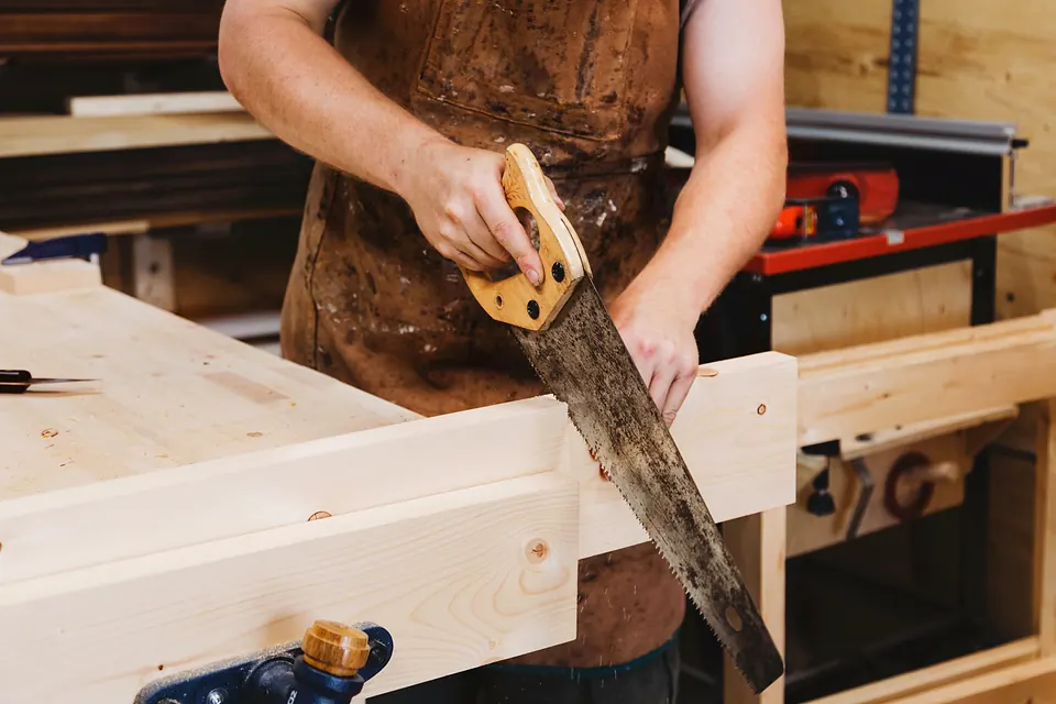 A woodworker cutting timber with a handsaw at a workbench