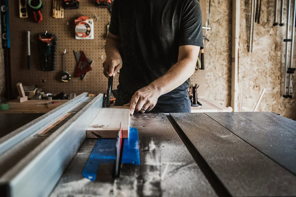 A carpenter cutting wood on a table saw in a workshop