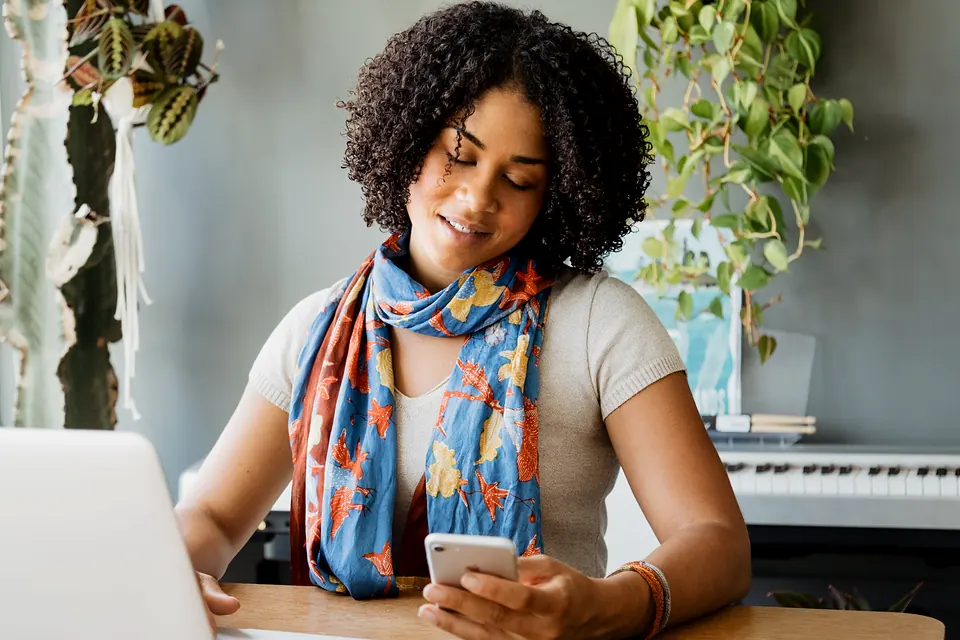 A woman in a bright scarf checking her phone at her desk