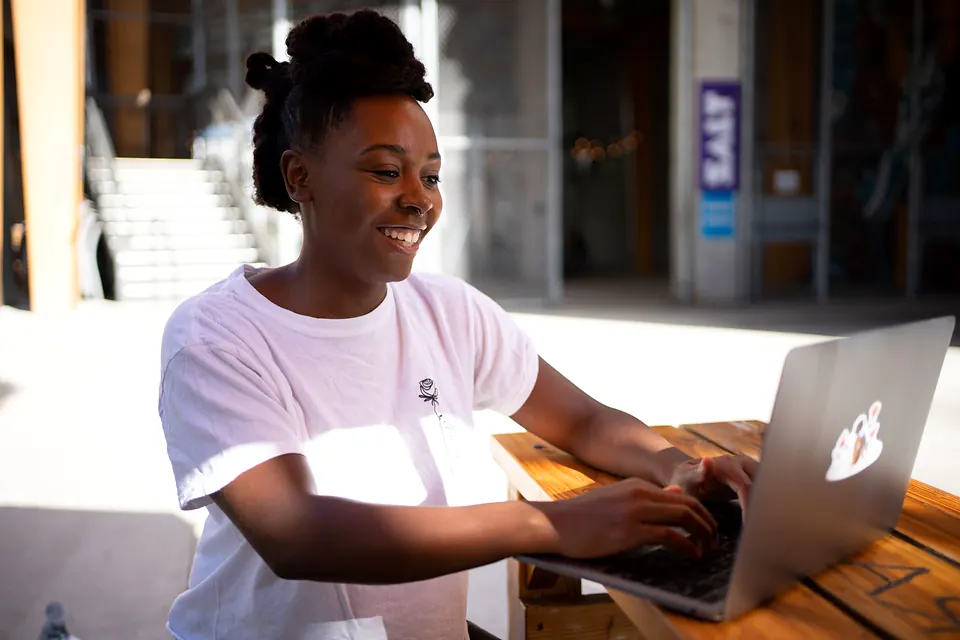 A woman laughing as she works on a laptop at a wooden table